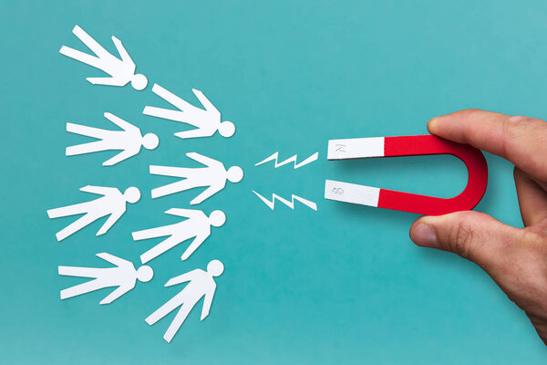 Крупный план человеческой руки, привлекающей белых людей с подковообразным магнитом на синем фоне
