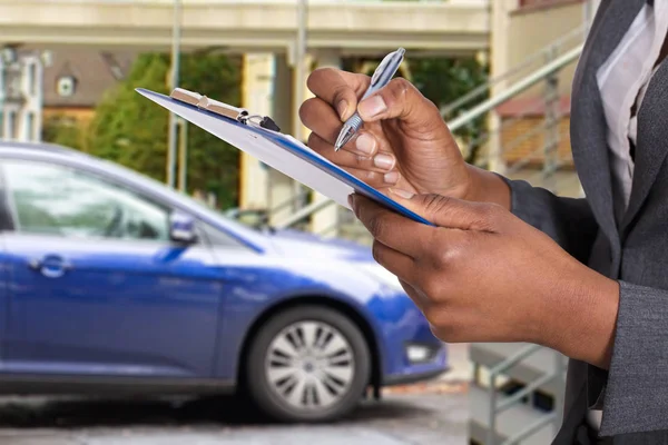 一名妇女手牵着写字板的特写镜头 该写字板上有保险单和一辆靠近蓝色轿车的钢笔 — 图库照片