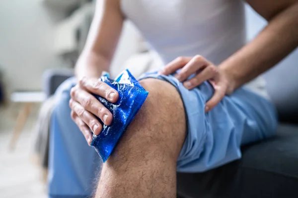 一个人在受伤的膝关节上坐着用冰块包的特写 — 图库照片