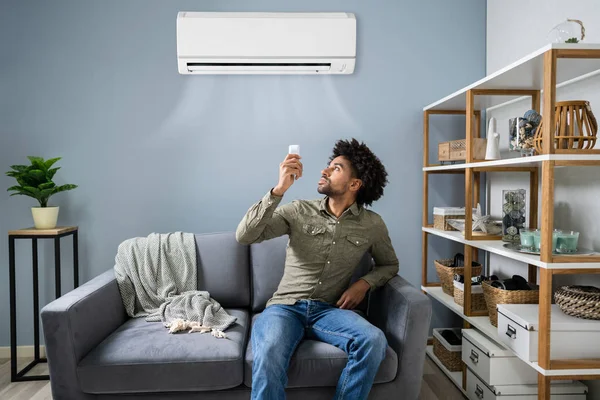 Joven Hombre Feliz Sentado Sofá Funcionamiento Aire Acondicionado Con Control — Foto de Stock