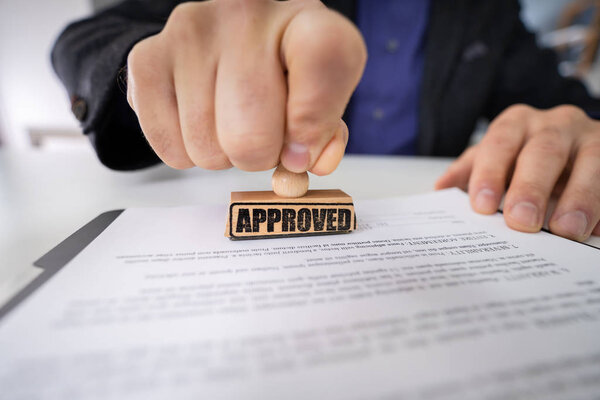 Close-up Of Person Hands Using Stamper On Document With The Text Approved