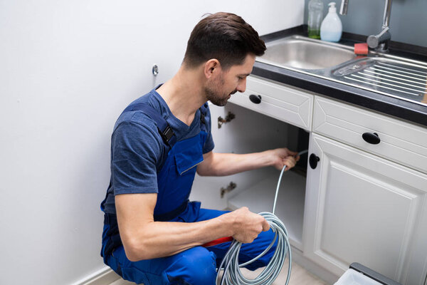 Male Plumber Cleaning Clogged Sink Pipe In Kitchen