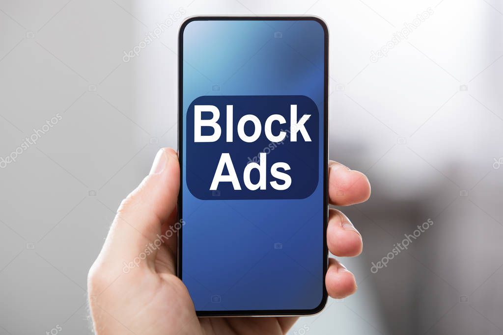 Person's Hand Holding Mobile Phone With Screen Showing Block Ads Message Against Blur Background