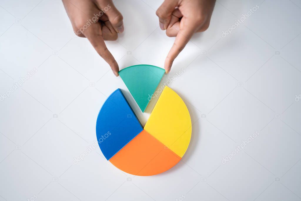 High Angle View Of Businessperson's Hand Placing A Last Piece Into Pie Chart