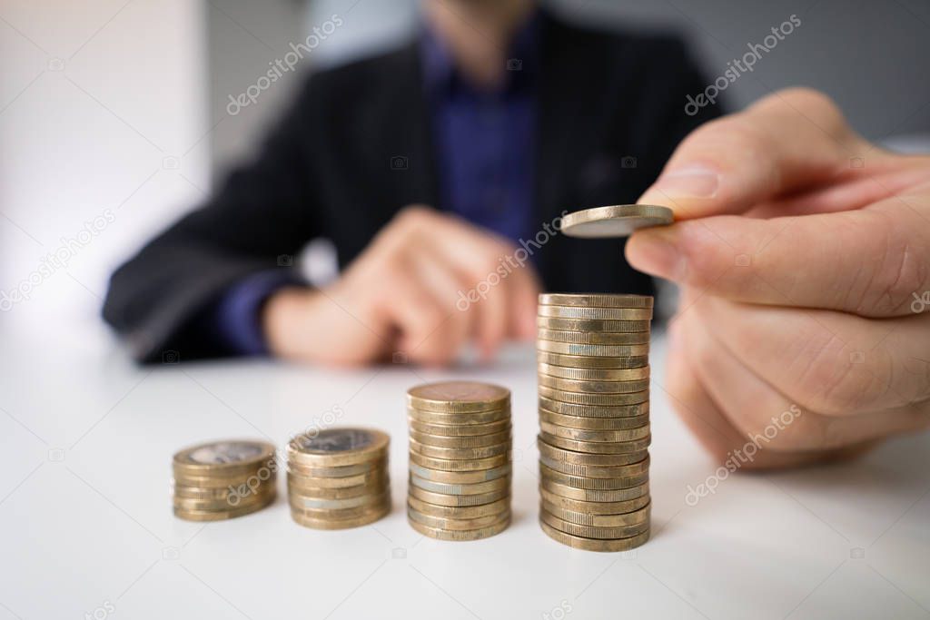 Close-up Of A Young African Businessman Stacking Coins On Desk