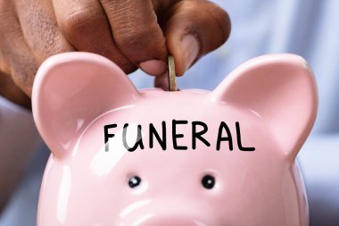 Cenaze için para biriktiren kişi domuz kumbarasına cenaze metniyle para sokuyor.