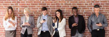 Tuğla Duvarı 'nın yanında duran Çeşitli İnsanlar Akıllı Telefon Kullanıyor