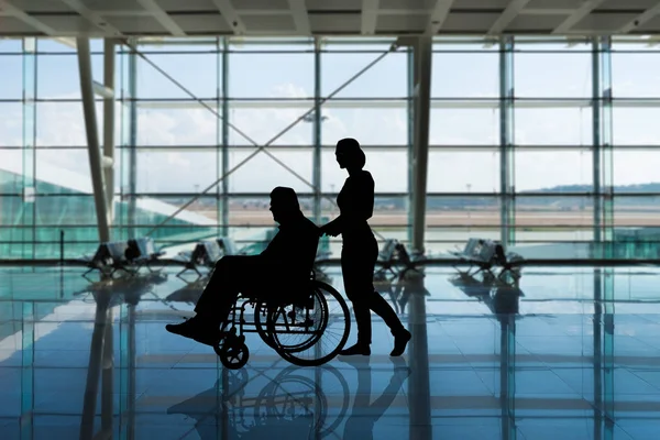 Sylwetka Kobiety Spacerującej Niepełnosprawną Osobą Wózku Inwalidzkim Lotnisku — Zdjęcie stockowe