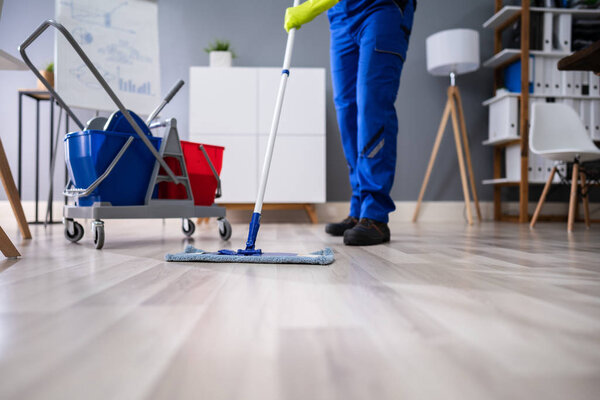 Счастливый молодой человек моет пол шваброй в современном офисе
