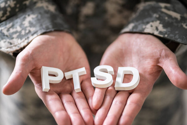 Close-up Of Male Soldier In Military Uniform Holding Wooden Cubes With PTSD Text