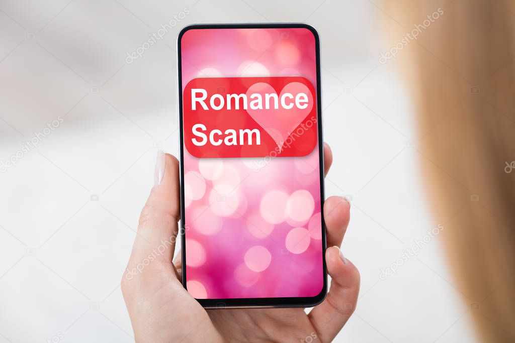 Close-up Of A Female's Hand Holding Mobile Phone With Romance Scam Application On Screen