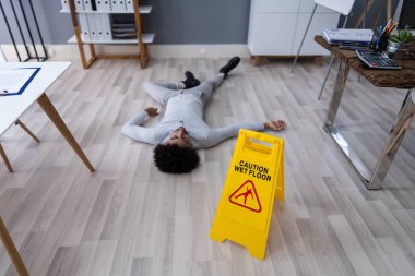 Ofisteki Dikkat Tabelasının önünde ıslak zemine düşen olgun bir adam.
