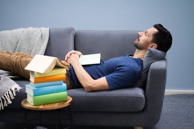 Adam evde kitapla birlikte kanepede uyuyor.