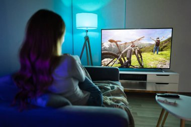 Evde televizyon film izlerken halı üzerinde oturan genç kadın