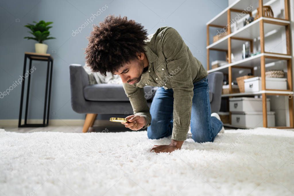 Side View Of A Young Male Janitor Looking At Carpet With Magnifying Glass