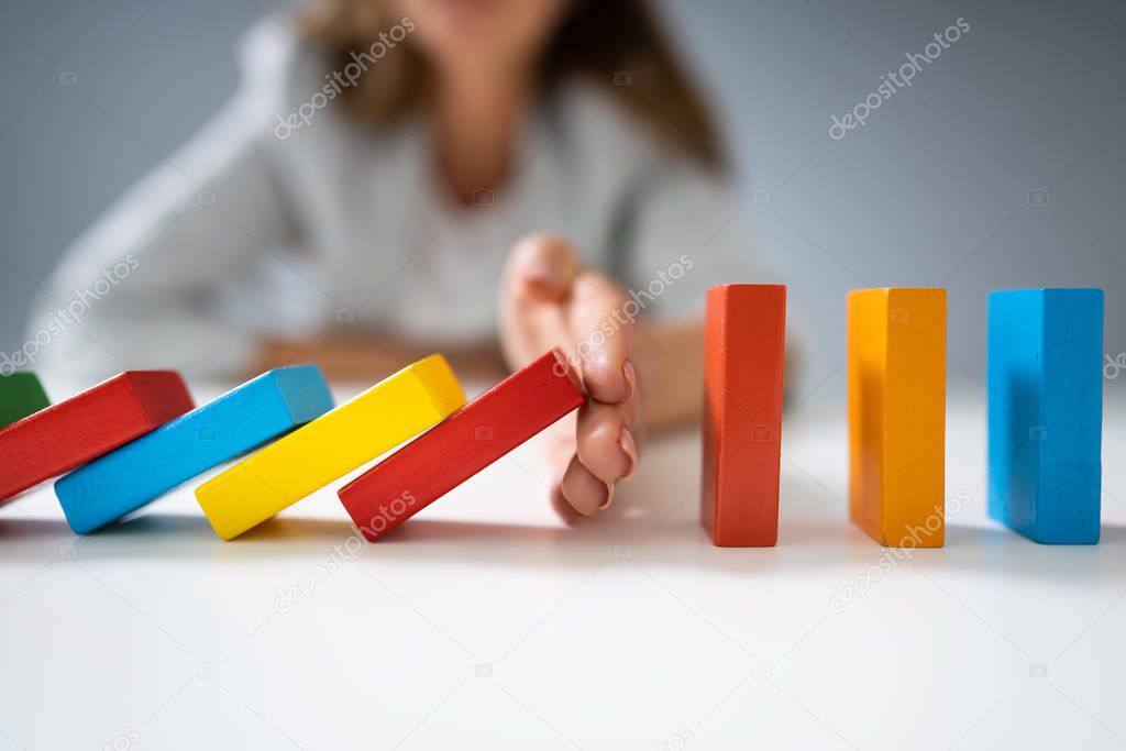 High Angle View Of A Businessperson Stopping Colorful Dominoes From Falling On Desk