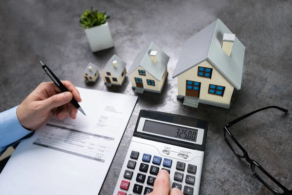 Biznesmen Obliczanie Podatku Przez Małe Duże Modele Domów — Zdjęcie stockowe