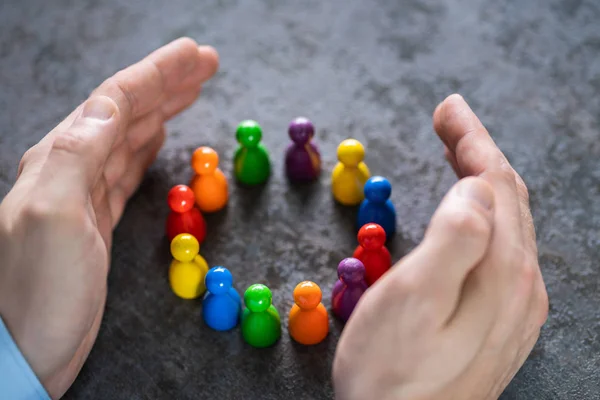 Close Person Hand Protecting Multicolored Pawns Forming Circle White Desk — Stock Photo, Image