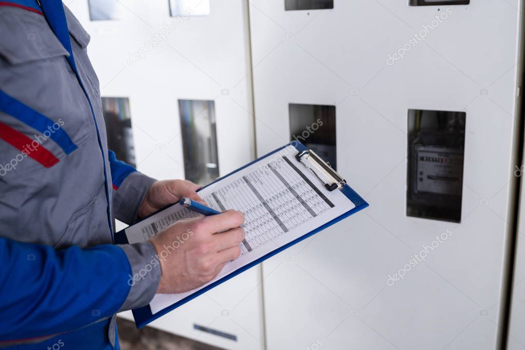 Close-up Of A Technician Hand Writing Reading Of Meter On Clipboard