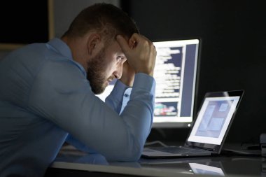 Endişeli programcı çoklu bilgisayar ekranlarında gece geç saatlere kadar çalışıyor