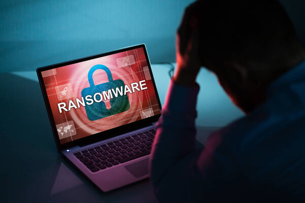 Беспокойный бизнесмен, глядя на ноутбук со словом Ransomware на экране на рабочем месте

