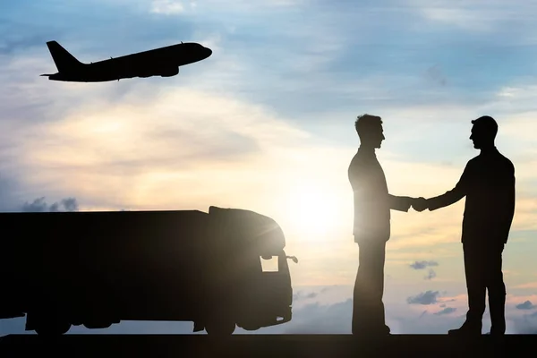 日没の間に商用トラックや航空機の近くで手を振る2人のビジネスマンのシルエット — ストック写真