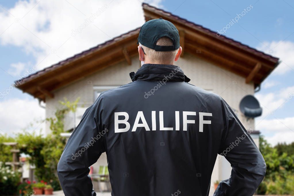 Rear View Of A Male Bailiff Standing With His Hands On Hips At House Entrance