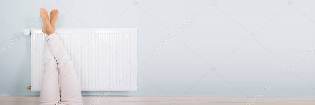 Young Woman Warming Up Legs On White Radiator
