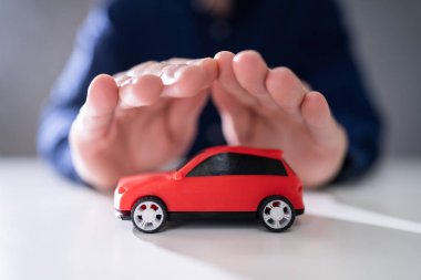 Yansıtıcı masada kırmızı oyuncak araba koruyan işadamı el