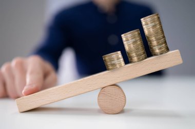 Close-up Of A Businessperson Balancing Increasing Stacked Coins With Finger On Seesaw clipart