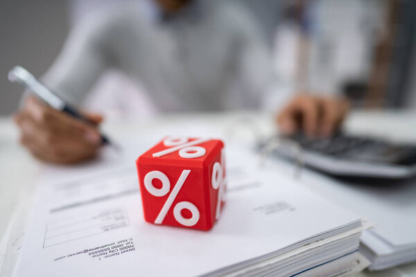 Крупный план красного кубического блока с символом процента перед лицом расчета счета-фактуры предпринимателя
