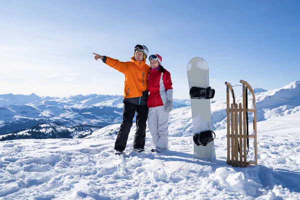 雪板の近くに立つ幸せなカップルの肖像画と雪の中の木製のそり — ストック写真