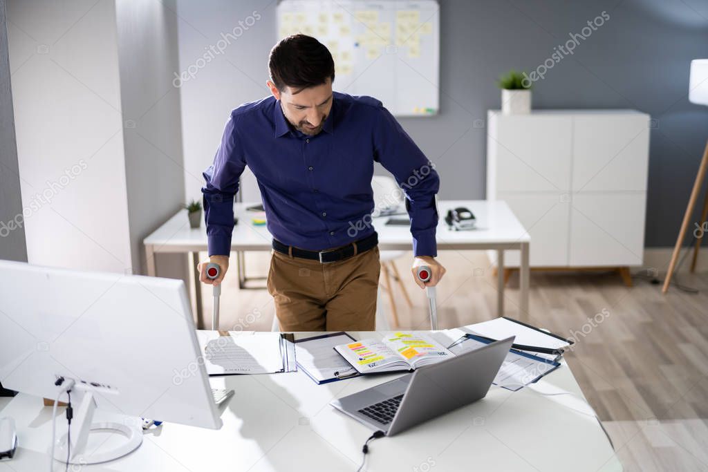 Handicapped Businessman Walking On Hardwood Floor With Crutches At Workplace