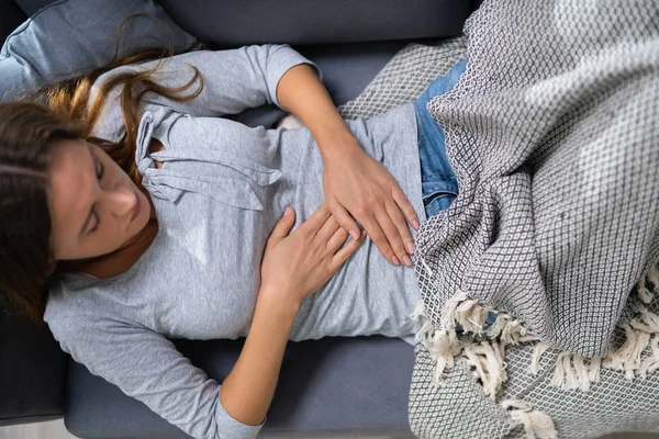 自宅でソファに腹痛に苦しんでいる若い女性の高角度のビュー — ストック写真