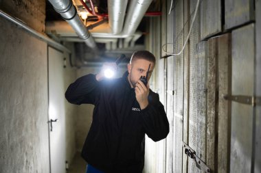 Rear View Of A Security Guard Standing In The Basement Holding Flashlight clipart