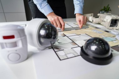 Bir mimarın elinin, masasında güvenlik ekipmanı olan planının yakın plan resmi.