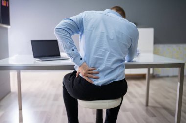 Ofis masasında otururken sırtı ağrıyan genç iş adamı