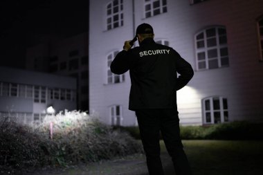 Gece vakti el feneriyle bina çevresi güvenlik görevlisi geziyor.