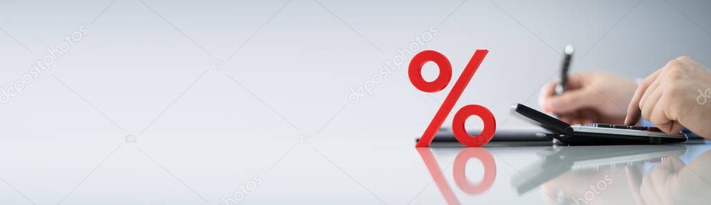 Close-up Of Red Percentage Symbol In Front Of Businessperson Calculating Invoice