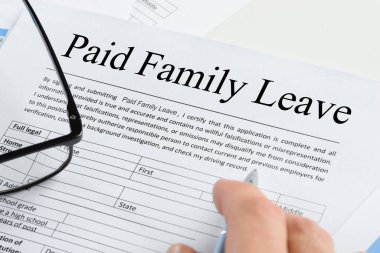 Close-up Of A Person's Hand Holding Pen Over Paid Family Leave Form With Spectacles clipart