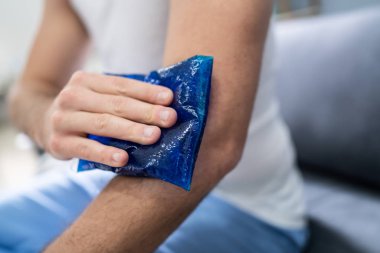 Bir adamın elinin koluna buz jeli sürerken yakın plan çekimi.