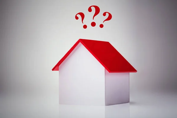 Kleines Hausmodell Mit Roten Fragezeichen Über Reflektierendem Schreibtisch Vor Grauem — Stockfoto