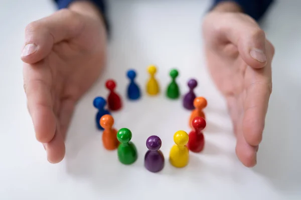 Close Person Hand Protecting Multicolored Pawns Forming Circle White Desk — Stock Photo, Image