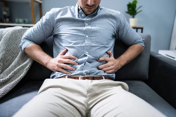 自宅でカウチに座って胃の痛みを持つ男 — ストック写真