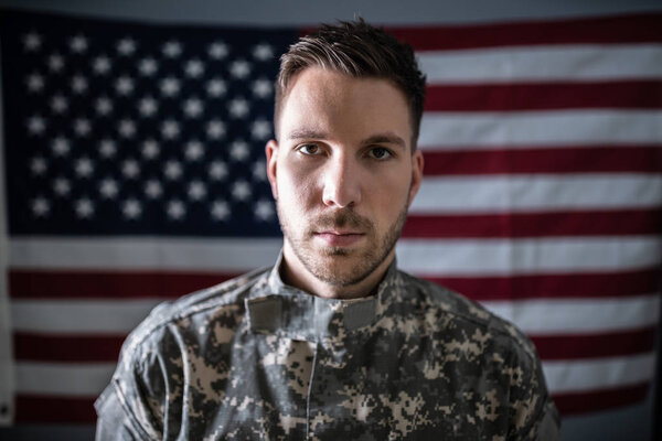 Portrait Of Serious Solider Standing In Front Of Us Flag