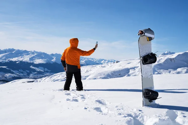 Mężczyzna Robi Zdjęcia Telefonu Komórkowego Przez Śnieżny Krajobraz Pobliżu Snowboardu — Zdjęcie stockowe