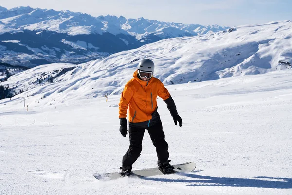 Happy Young Male Snow Boarder Enjoying Riding Snow Board On Track Against Snowcapped Mountains