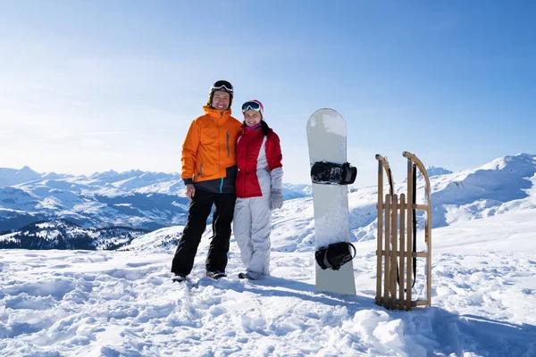 站在雪板旁边的一对快乐的年轻夫妇和在雪地里的木制誓言的画像 — 图库照片