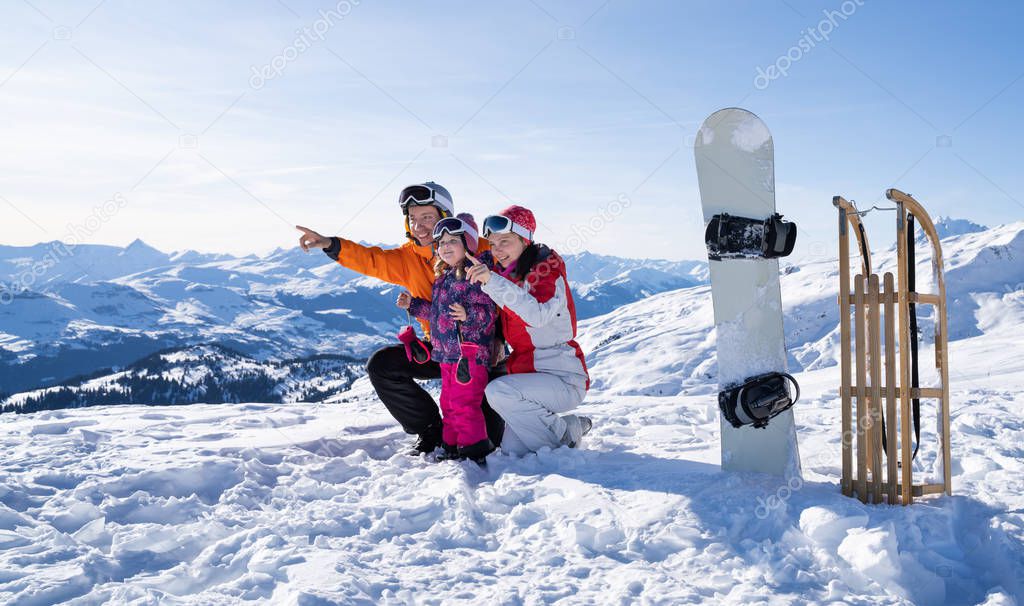 Smiling Couple Showing Something To Their Cute Little Daughter By Pointing Near Snowboard And Sledge