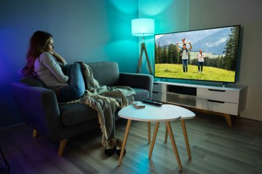 Evde televizyon film izlerken halı üzerinde oturan genç kadın
